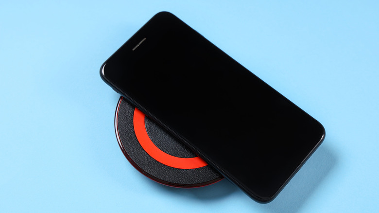An unknown smartphone with a front-firing speaker on a wireless charging pad, blue background