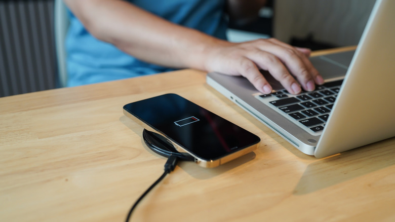 An older iPhone on a wireless charger, person using a laptop next to it