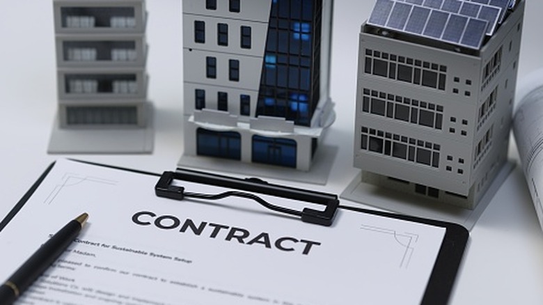 Models of buildings with solar panels behind a clipboard with the word "Contract" at the top and a pen sitting on top