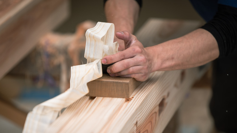 Man peeling off layers from plank of wood