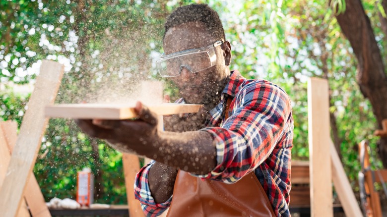 Inspecting a wooden board for a project with sawdust in the air.