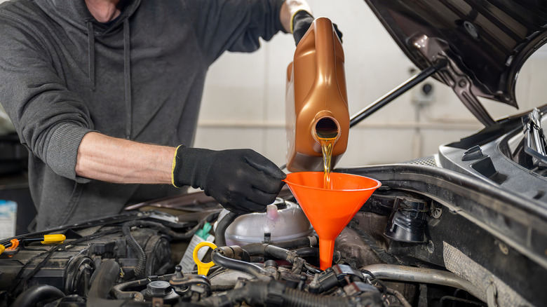 Person pours new gas under hood of car