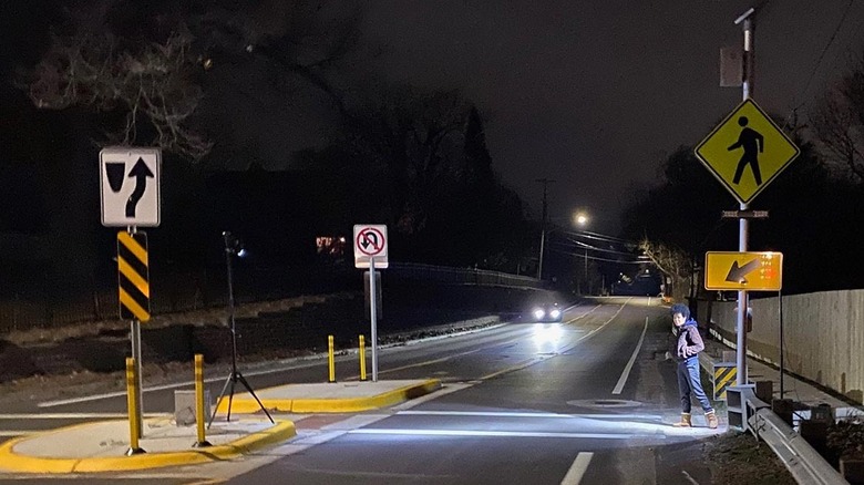 Pedestrian waiting at a lighted crosswalk at night as a car approaches