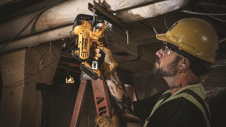 A worker in a hard hat and high-vis safety gear using a DeWalt 20V Max Threaded Rod Cutter.