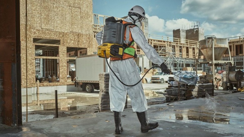 A worker on a jobsite, in full protective gear, using DeWalt's 20V Max XR Concrete Chemical Sprayer.