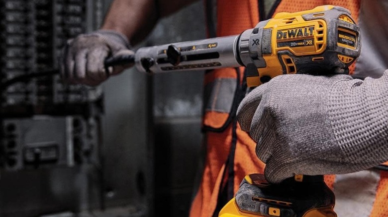 A worker gripping a DeWalt cordless cable stripper in front of a breaker box.