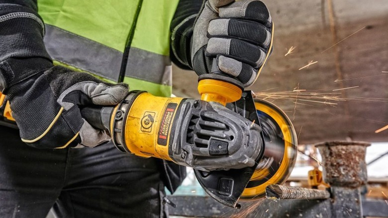 A worker using DeWalt's 60V Max Side Handle Detect Grinder to trim rebar.
