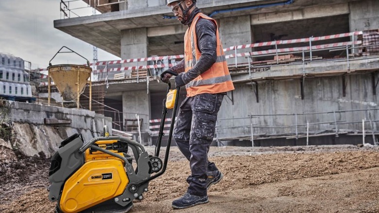 A worker on a jobsite, dressed in high-vis safety gear, using the DeWalt PowerShift Forward Plate Compactor.