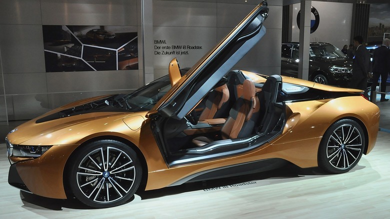 A brown BMW i8 on display in a BMW dealership showroom.