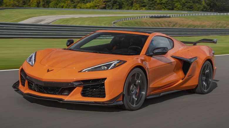 An orange 2024 Chevrolet Corvette Z06 speeds along a racetrack, showing off its aggressive front end and rear wing.