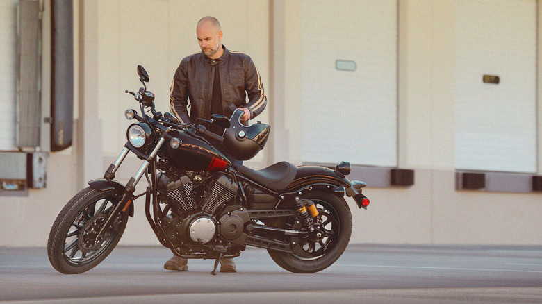 A man carrying a helmet looks at the speedometer on a parked Yamaha Bolt.
