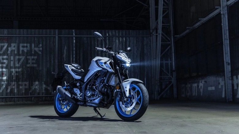 A light colored Yamaha MT-03 with its LED light on parked at night