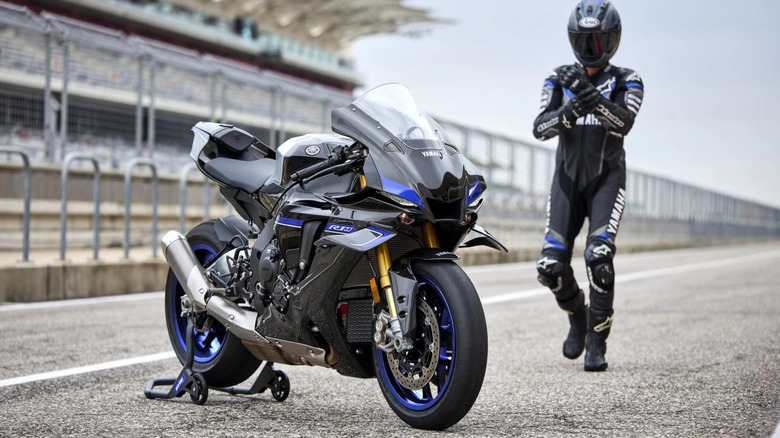 Rider approaching a parked Yamaha R1-M in a pit lane
