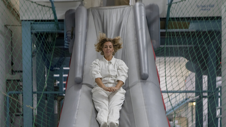 A woman in a white jumpsuit with blond hair sliding down an inflatable slide during a mock evacuation drill
