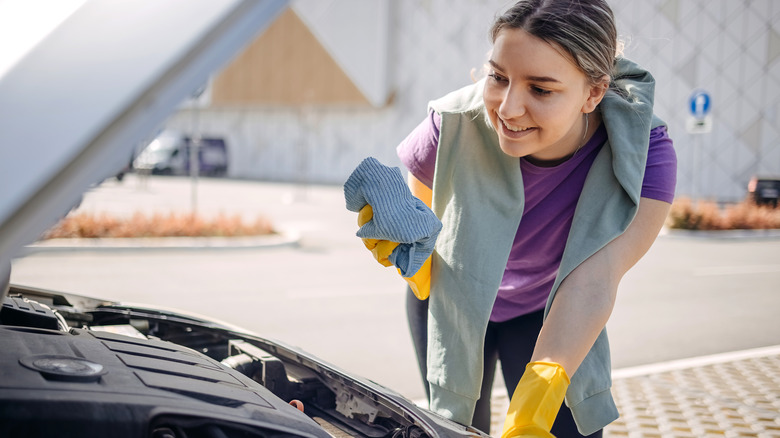woman holding rag leaning over car with open hood