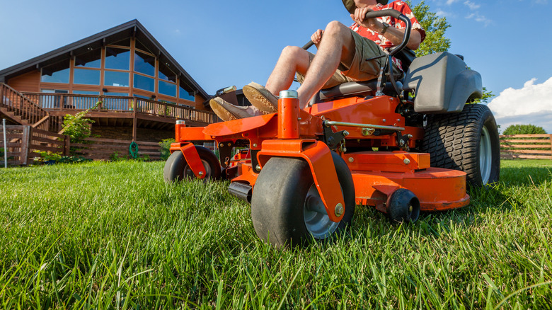 A person using an orange zero turn riding lawn mower