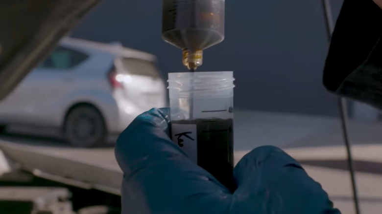 Oil from an engine getting siphoned into a plastic test container