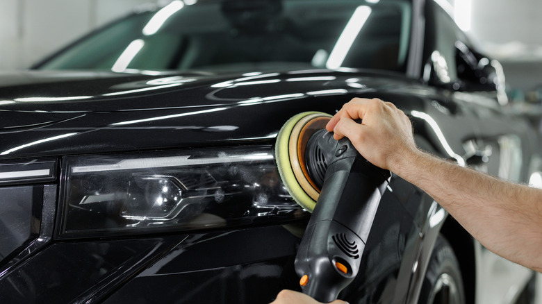 A black car's headlight and front bumper area being buffed and polished