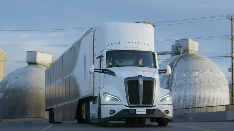 A front on photo of the new Kenworth T680E electric semi truck driving up a road.