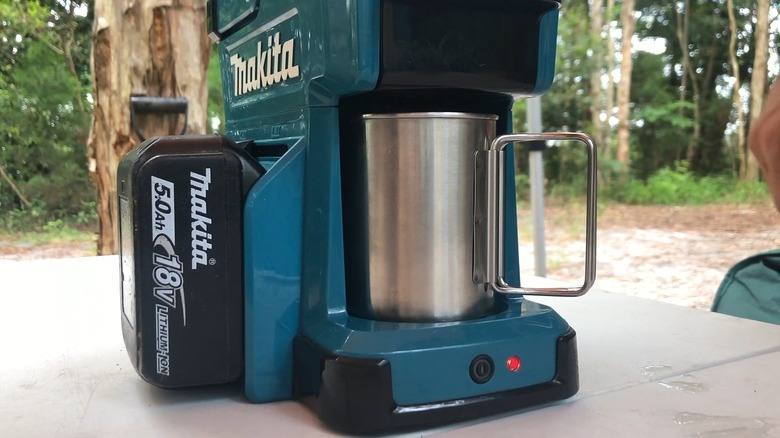 A Makita Cordless Coffee Maker with cup at campground