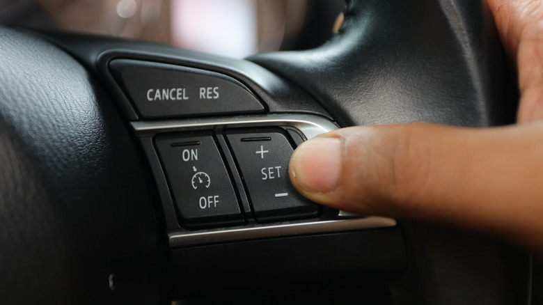 A closeup of a driver's hand setting the cruise control with buttons on the steering wheel