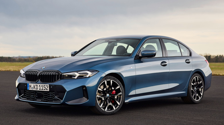Front 3/4 view of BMW 330i on tarmac in grassy, forested area