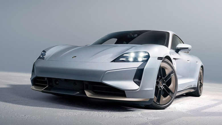 Front view of a silver Porsche Tacycan with lights on.
