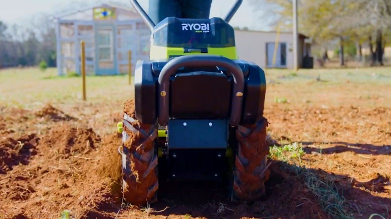A person using a Ryobi tiller on dirt.