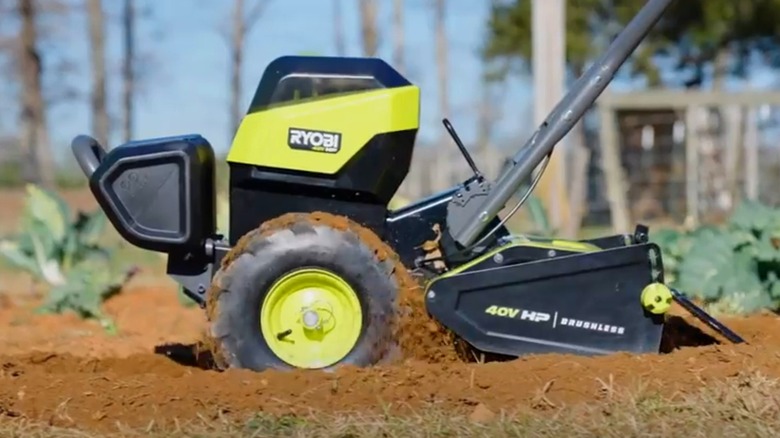 A person using a Ryobi rear tine tiller on soil.