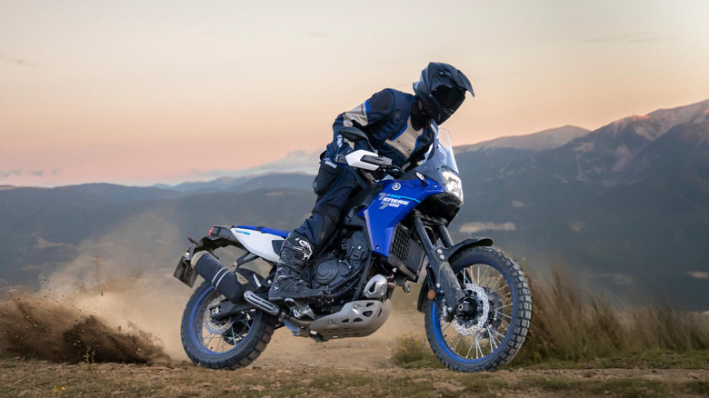 A side shot of a person sliding a Yamaha Tenere 700 on a dirt trail with mountains in the background