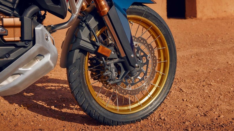 Close-up of a motorcycle front wheel and tire with a gold spoked rim
