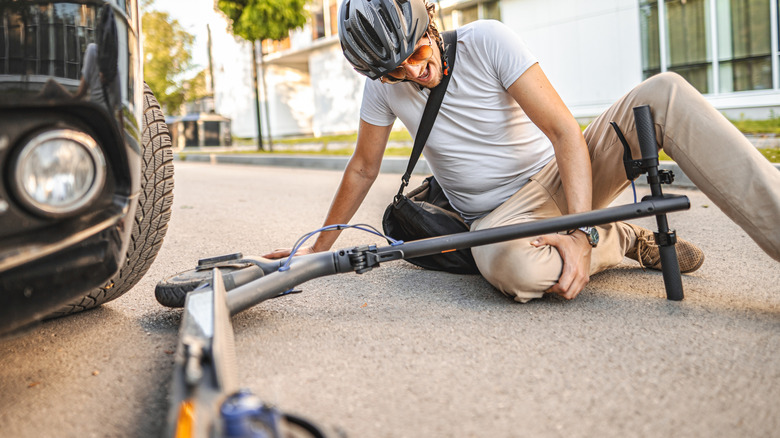 man with helmet feels his knee after e-scooter accident