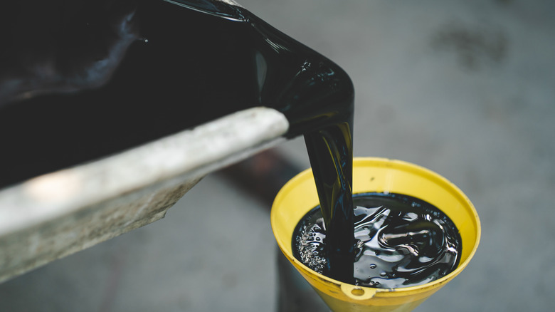 Spent black motor oil being transferred from a pan to a funnel