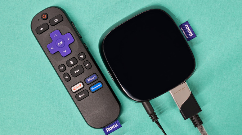 A Roku device and remote against a teal background.