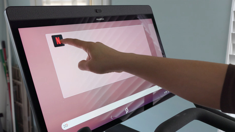 Person tapping the Netflix logo on a Peloton