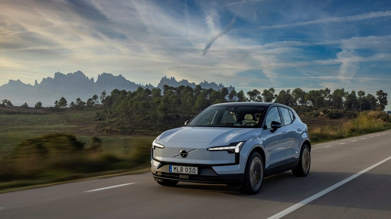 LIght blue Volvo EX30 on highway with mountains and trees in background