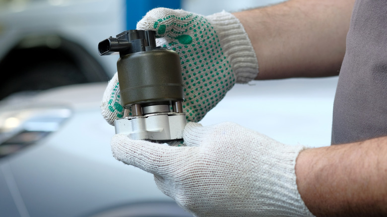 A gloved mechanic holding a new EGR valve, preparing it for installation
