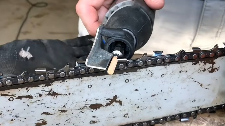 A person sharpening a chainsaw with a rotary tool.