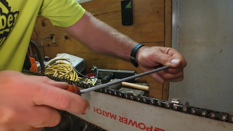 A person sharpening a chainsaw chain by hand.