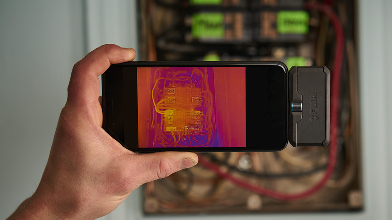 Hand holding a phone with FLIR ONE thermal camera connected