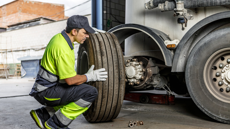 A mechanic in a green and gray uniform getting ready to mount a tire on a truck