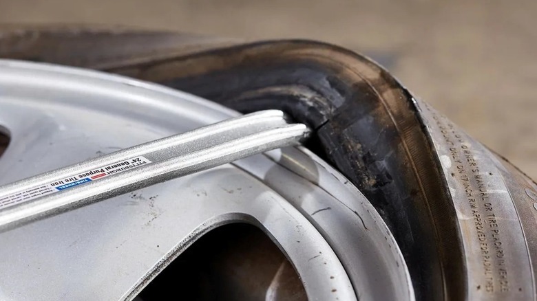 Using a tire spoon to pull the tire bead over the edge of the wheel when dismounting a tire.