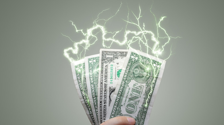 A hand holding dollar bills with electric sparks coming out of them