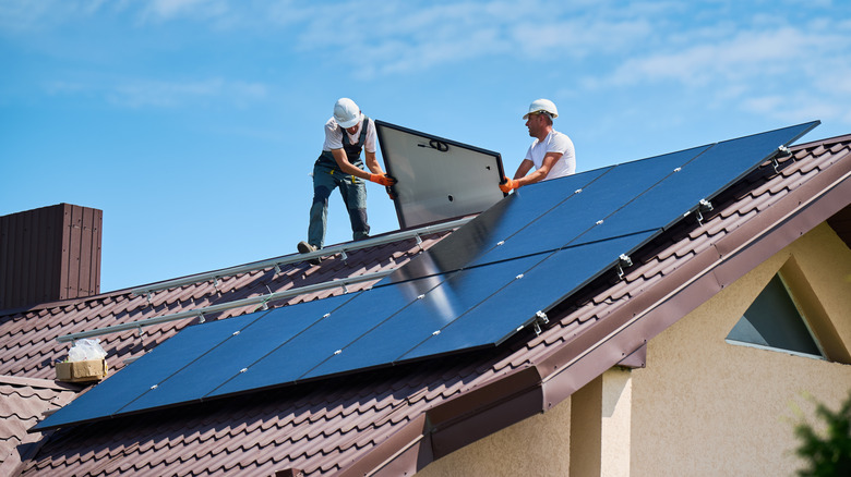 Two workers install solar panels on the roof of a home