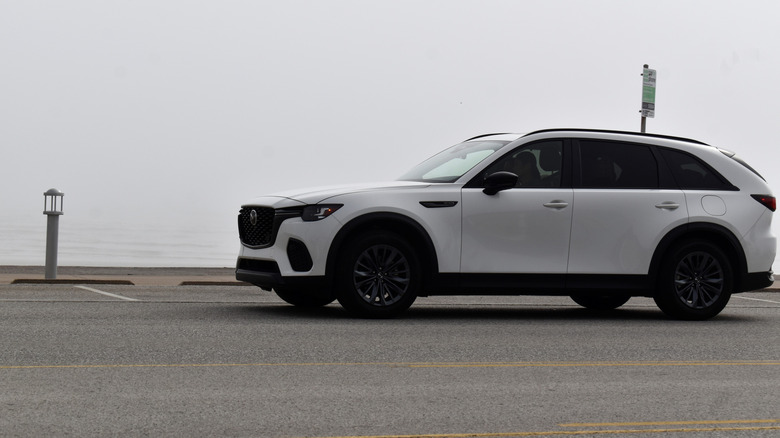 White Mazda CX-90 driving by a body of water