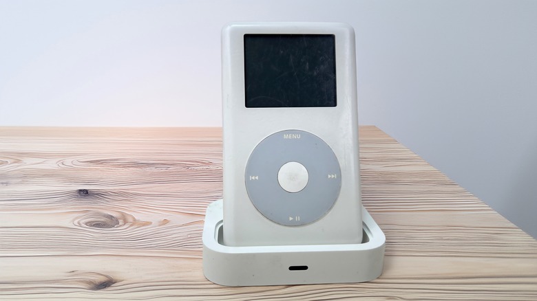An Apple iPod classic on a charging stand atop a wooden table.