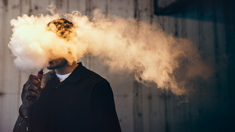Young man covered in cloud of vape smoke