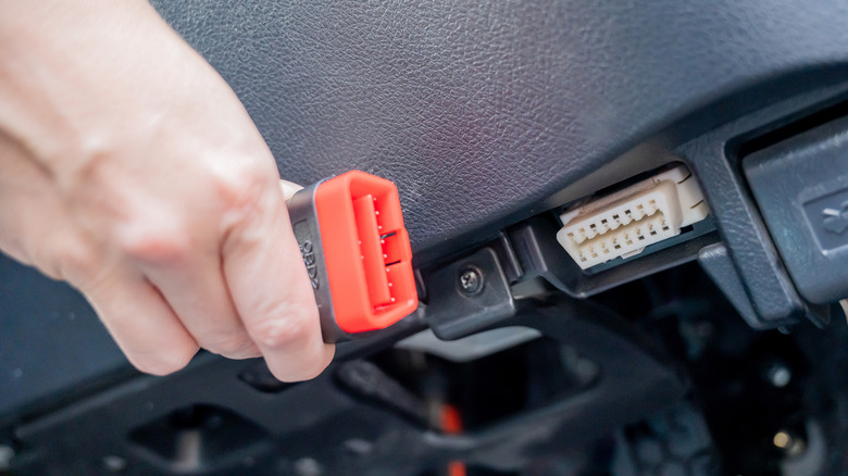 A person preparing to plug in an OBD-II scanner into an unidentified car's OBD-II port