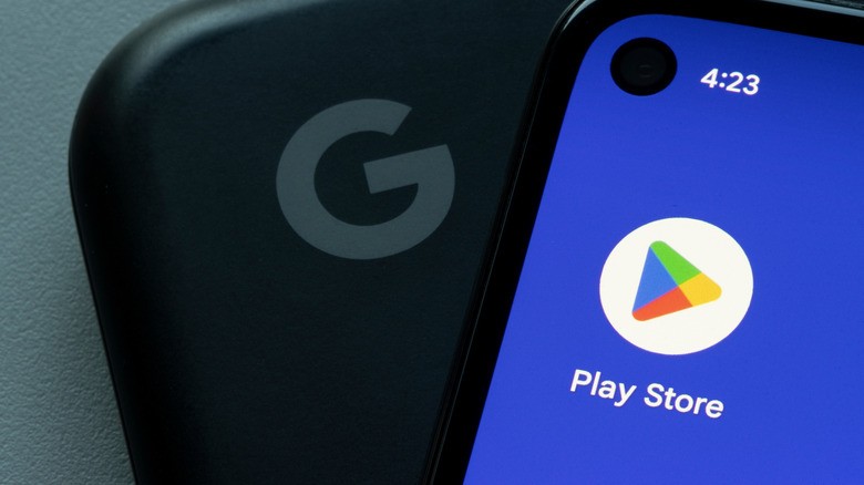 Google Play Store app icon is seen on a Google Pixel smartphone atop a Google Pixelbook