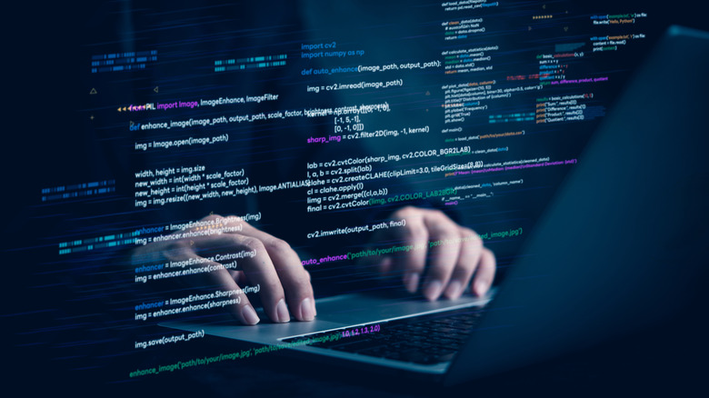 Hands typing on a laptop with code displayed on a transparent display